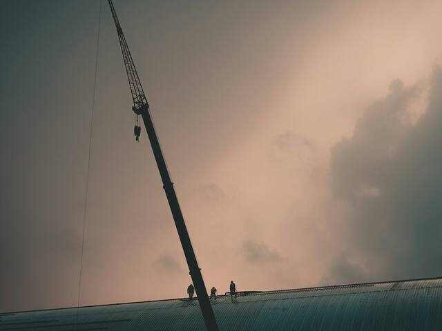 Three workers on the roof beside the crane boom.