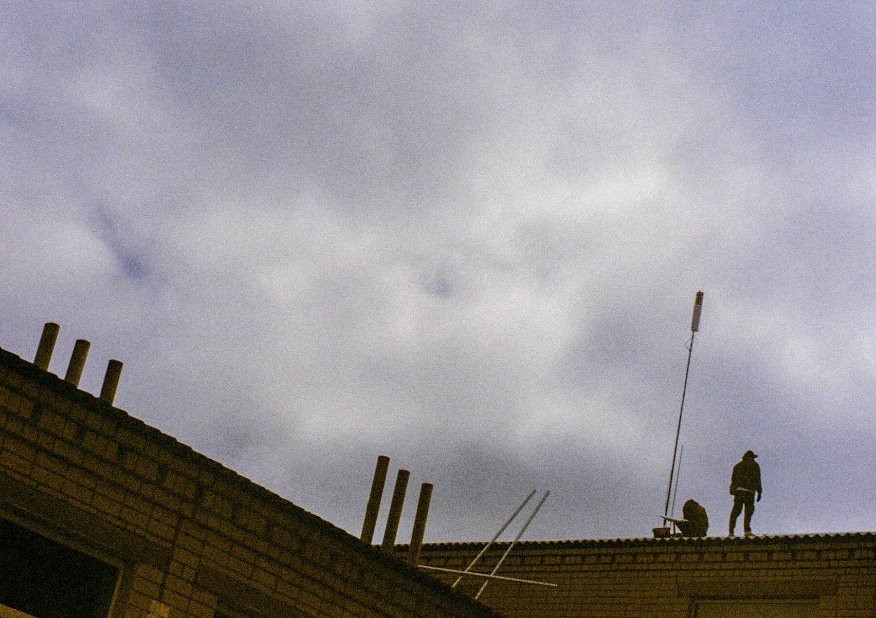 Two workers on a rooftop under a low, grey sky.